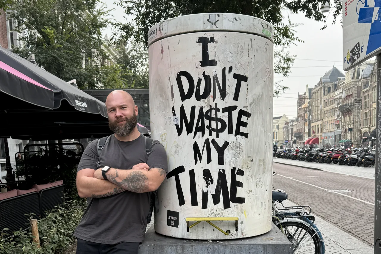 Tom standing with his arms folded beside a street artwork reading ‘I don’t waste my time’.